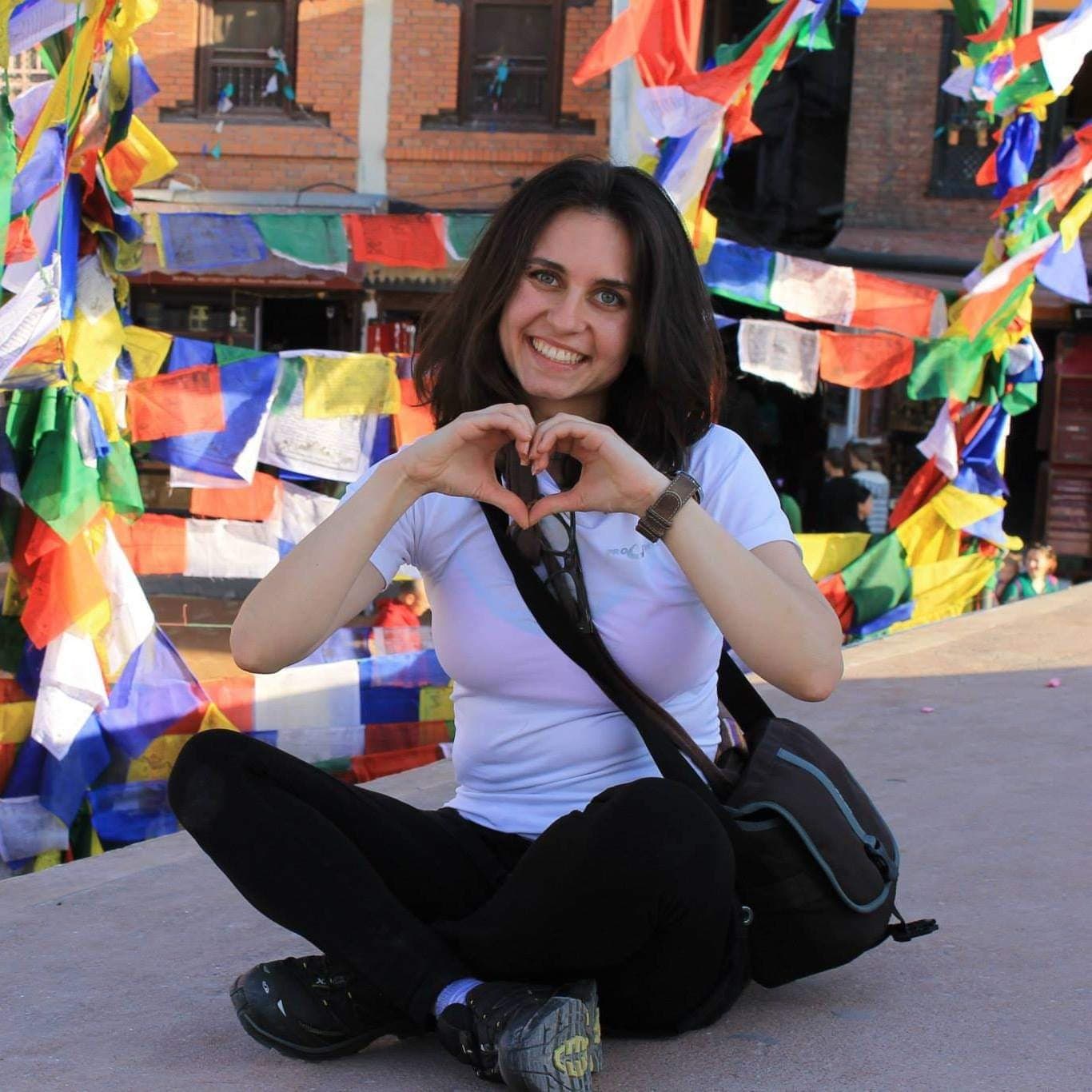 Elis smiling and making a heart with her hands under prayer flags