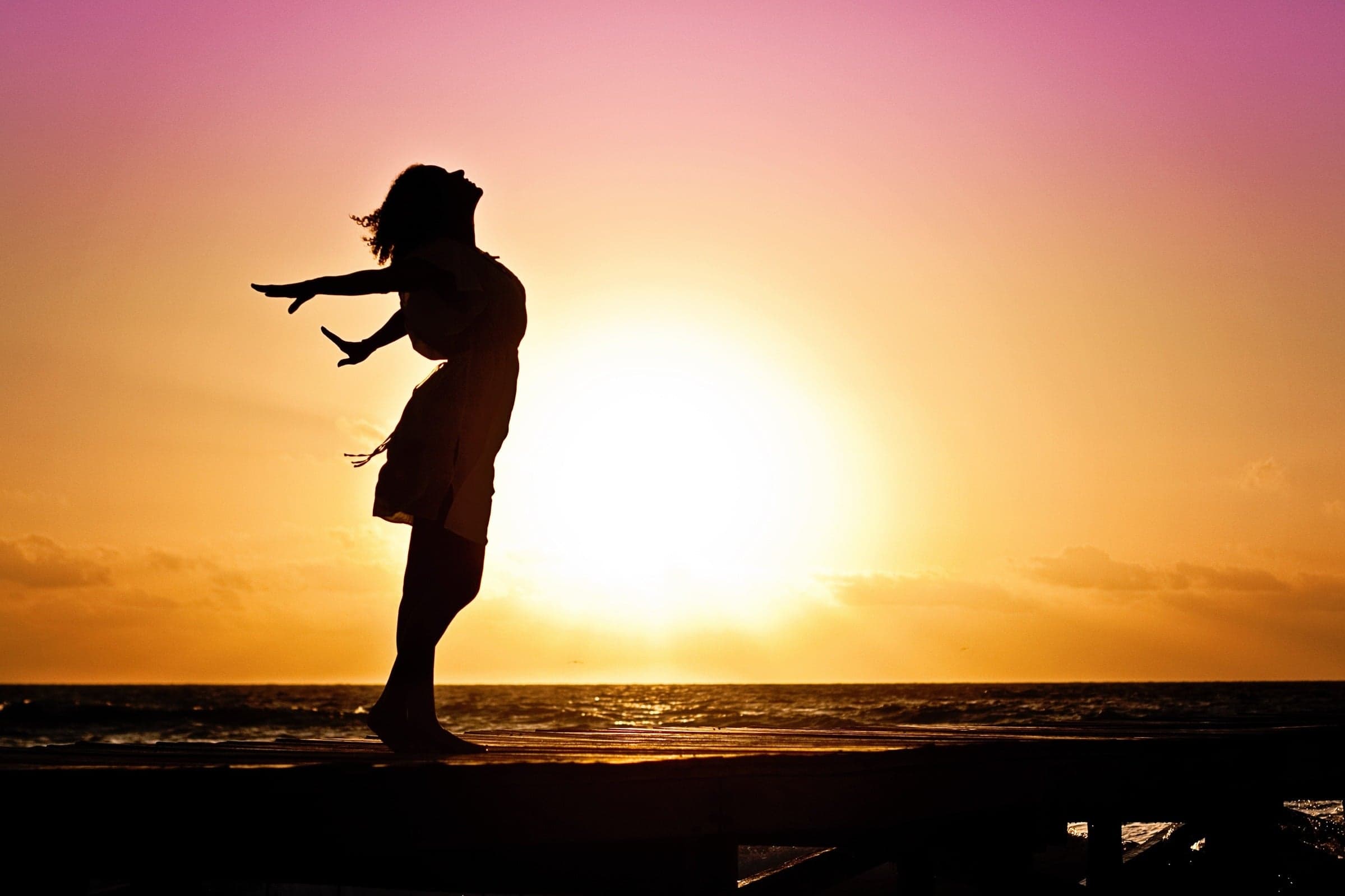 Silhouette of a woman with open arms at sunset