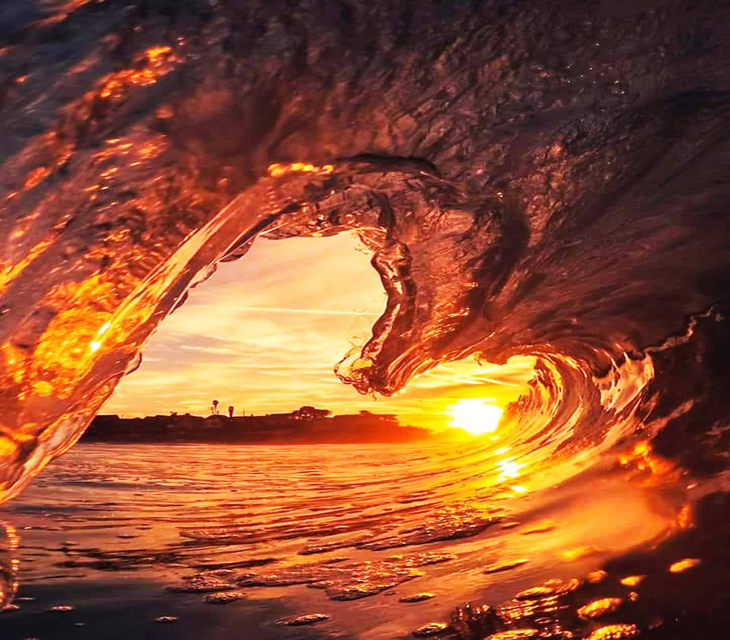A wave curling over the setting sun